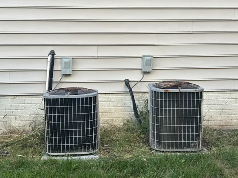 Before: Two older outdoor air conditioner units beside vinyl siding